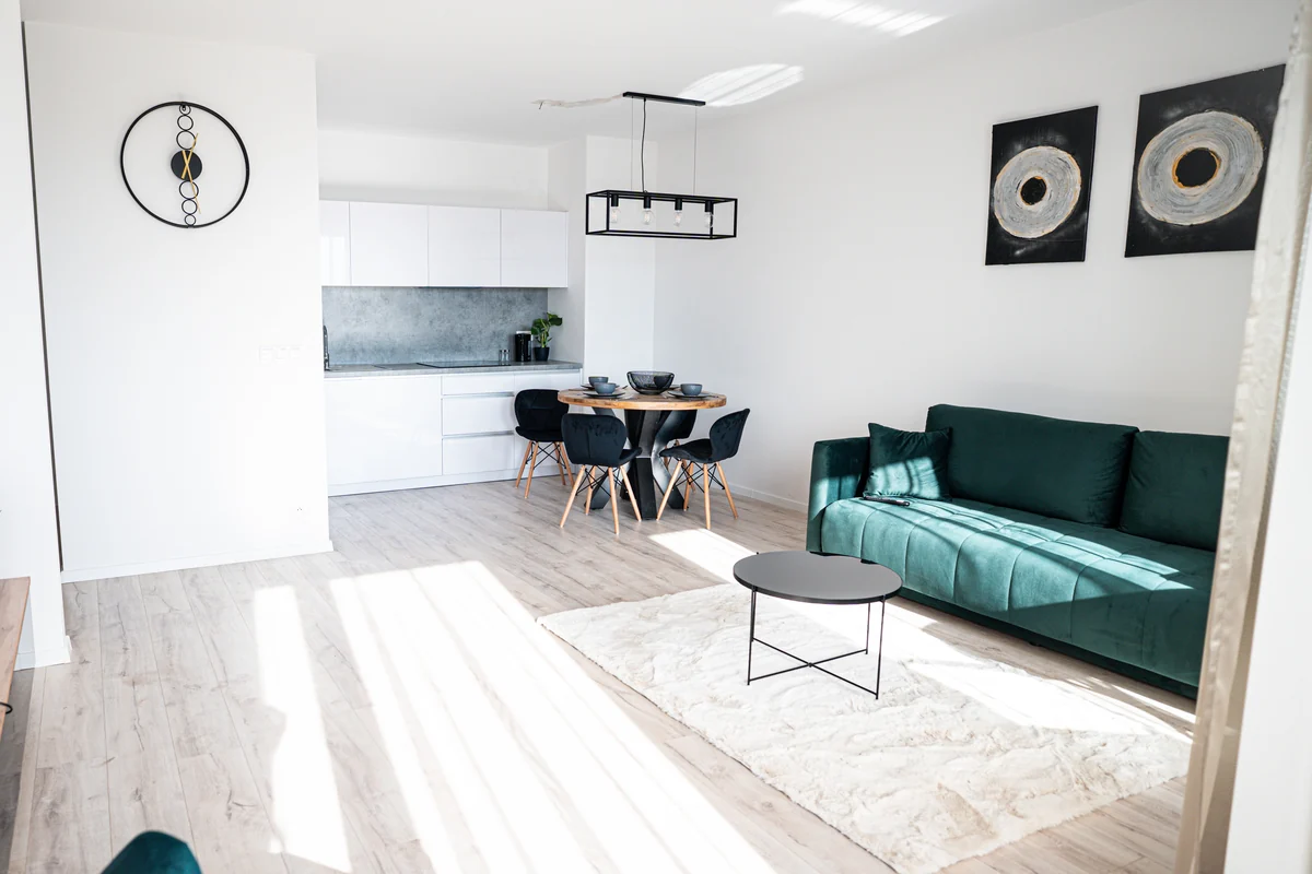 Obývačka apartmánu so zelenou sedačkou, jedálenským stolom a bielou kuchyňou