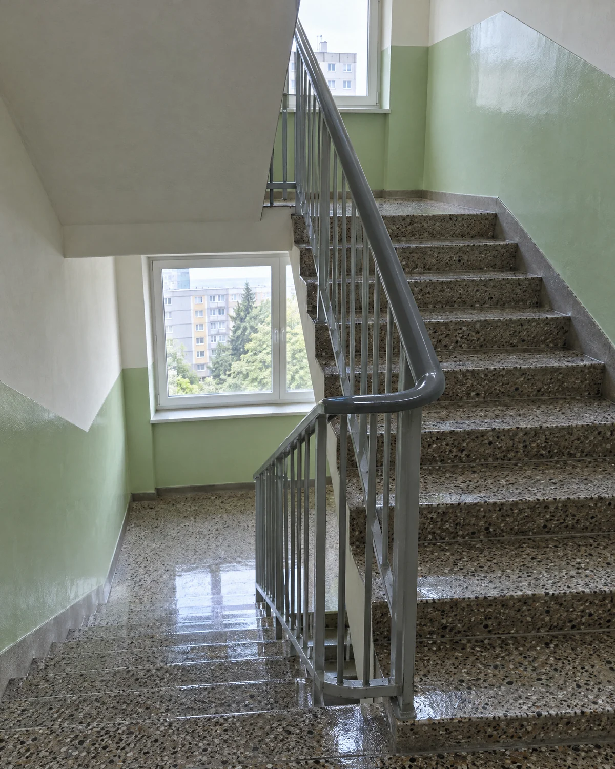 Umyté teracové schodisko so zábradlím a svetlozelenými stenami vo vchode bytového domu